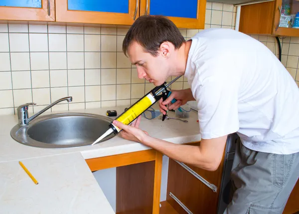 stock image Plumber putting a silicone sealant to installing a kitchen sink