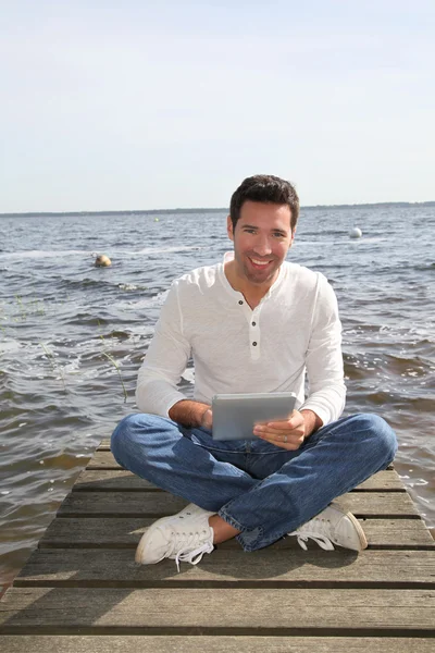 Handsome man sitting on a pontoon with touchpad — Stock Photo, Image