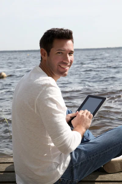 Hombre guapo sentado en un pontón con touchpad — Foto de Stock