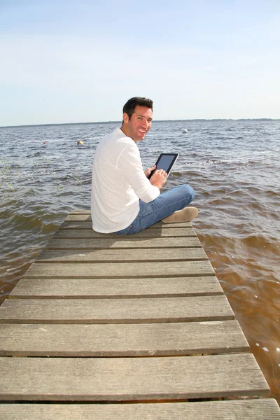 Schöner Mann sitzt auf einem Ponton mit Touchpad — Stockfoto
