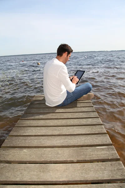 Handsome man sitting on a pontoon with touchpad — Stock Photo, Image