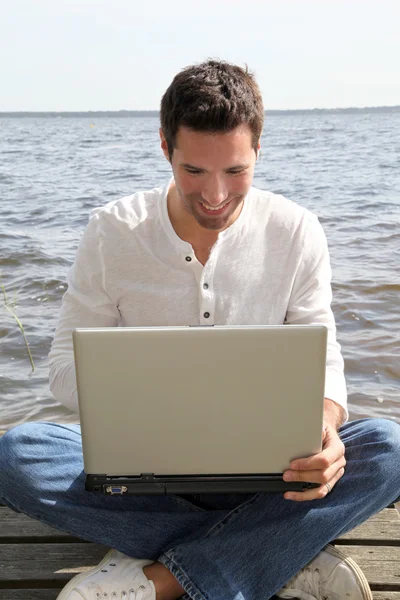 カップルは湖によって電子タブレットを使用して男子坐上浮桥与便携式计算机 — 图库照片
