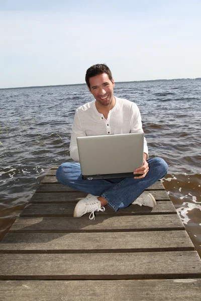 Muž sedí na pontonu s přenosným počítačem — Stock fotografie