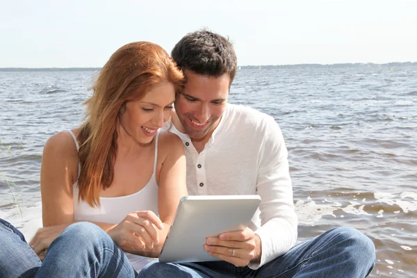 Pareja usando tableta electrónica junto a un lago —  Fotos de Stock