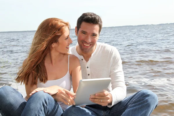 Pareja usando tableta electrónica junto a un lago — Foto de Stock