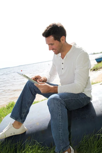 電子タブレットで湖畔に坐っている人 — ストック写真