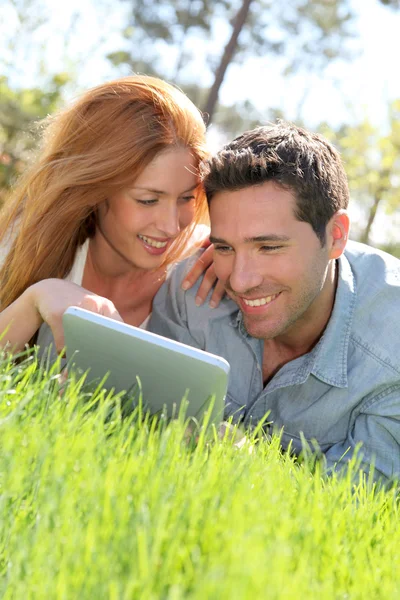 Paar legt sich mit Touchpad ins Gras — Stockfoto
