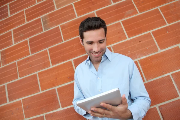 Uomo attraente utilizzando tablet elettronico appoggiato sul muro di mattoni — Foto Stock