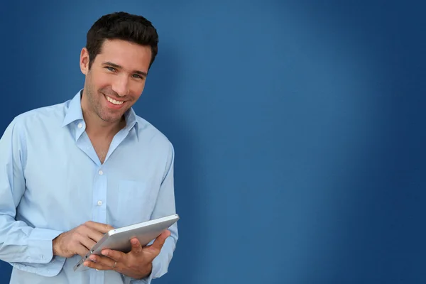 Homem atraente com touchpad no fundo azul — Fotografia de Stock