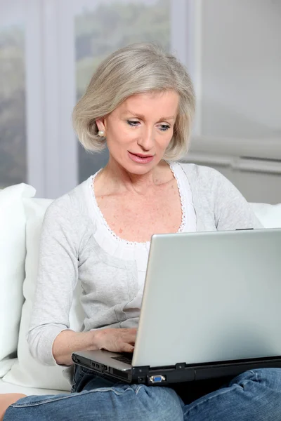 Старшая женщина сидит на диване с ноутбуком — стоковое фото