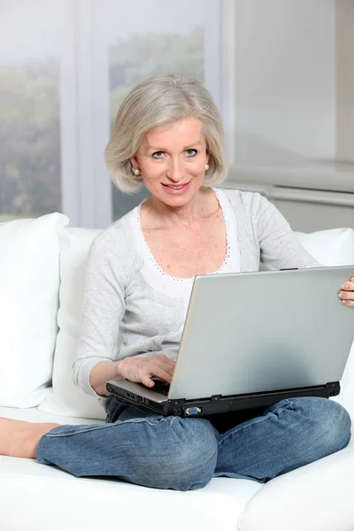 Starszy kobieta siedzi w kanapie z laptopem — Zdjęcie stockowe