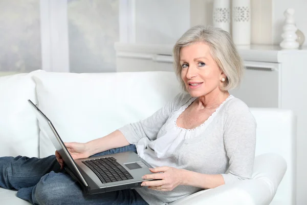 Mulher sênior sentada no sofá com computador portátil — Fotografia de Stock