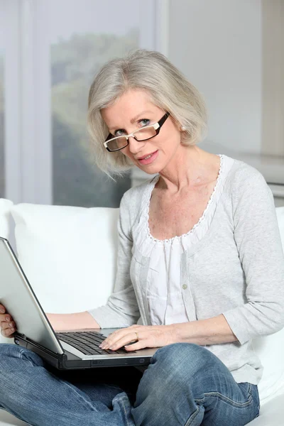 Mulher sênior sentada no sofá com computador portátil — Fotografia de Stock