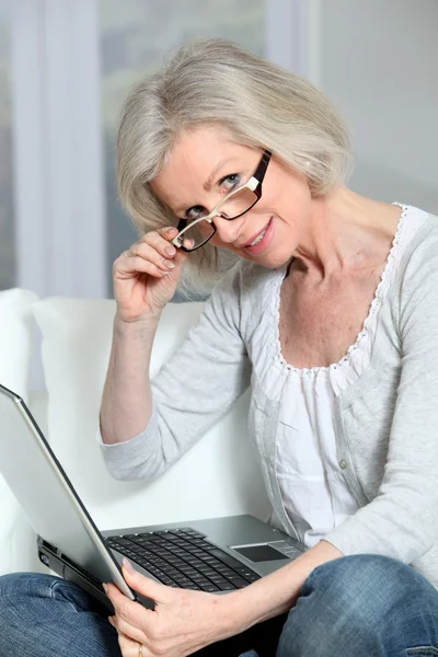 ラップトップ コンピューターでソファに座っている年配の女性 — ストック写真