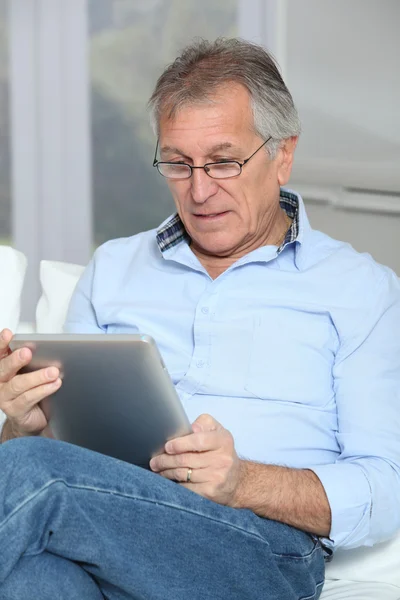 Äldre man sitter i soffan med elektroniska tablett — Stockfoto