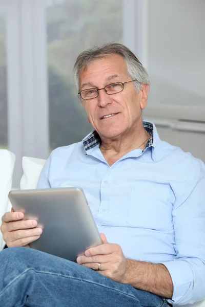 Старший мужчина сидит на диване с электронным планшетом — стоковое фото