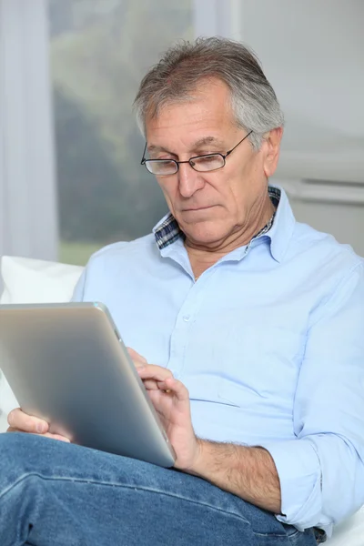 Старший мужчина сидит на диване с электронным планшетом — стоковое фото