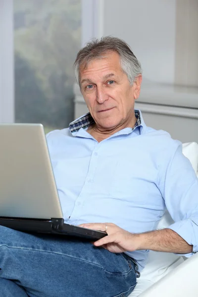 Homem sênior no sofá com computador portátil — Fotografia de Stock