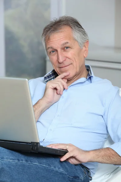 Uomo anziano in divano con computer portatile — Foto Stock