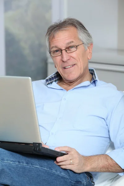 Starší muž na pohovce s notebookem — Stock fotografie