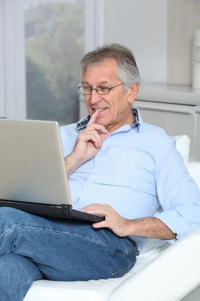 坐在沙发上拿着手提电脑的老人 — 图库照片