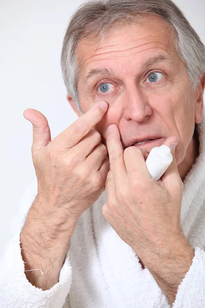 Senior mannen att sätta concealer runt ögonen — Stockfoto