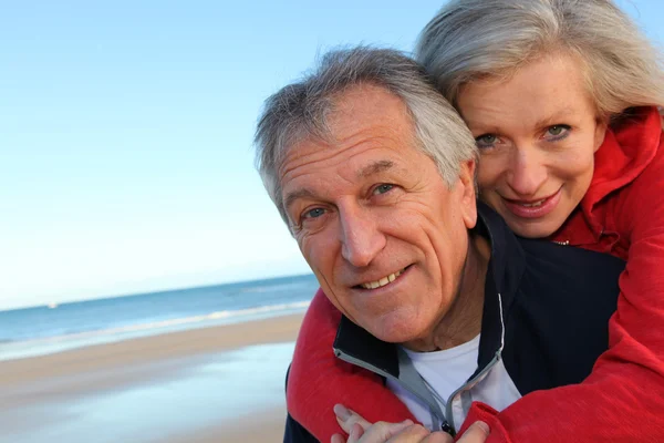 Senior Mann gibt Huckepack-Fahrt zu Frau am Meer — Stockfoto
