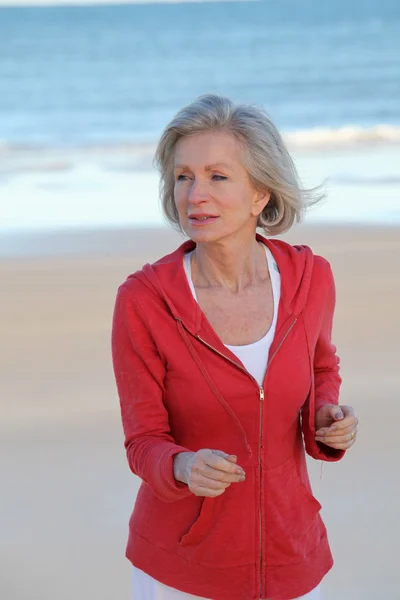 Старша жінка біжить на пляжі — стокове фото