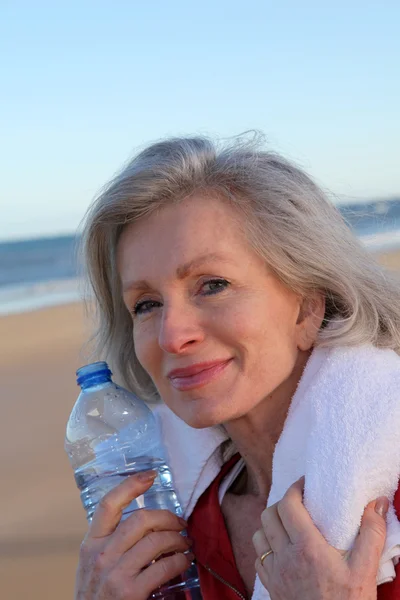 Actieve senior vrouw drinkwater uit de fles op het strand — Stockfoto