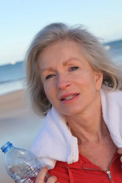 Aktive Seniorin trinkt Wasser aus Flasche am Strand — Stockfoto