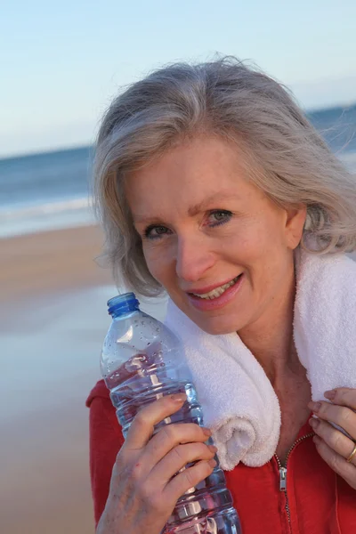 从瓶在海滩活动高级女人饮用水 — 图库照片