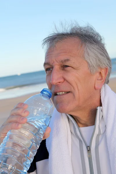 :Acqua potabile senior attiva dalla bottiglia in spiaggia — Foto Stock