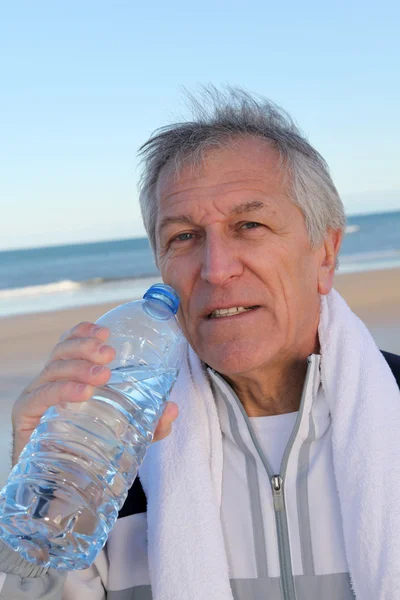 :aktif kıdemli içme suyu şişe sahilde — Stok fotoğraf