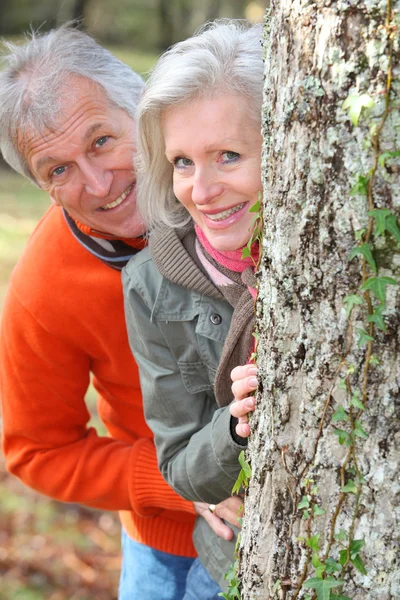 Encerramento de par sênior que se esconde atrás de uma árvore — Fotografia de Stock