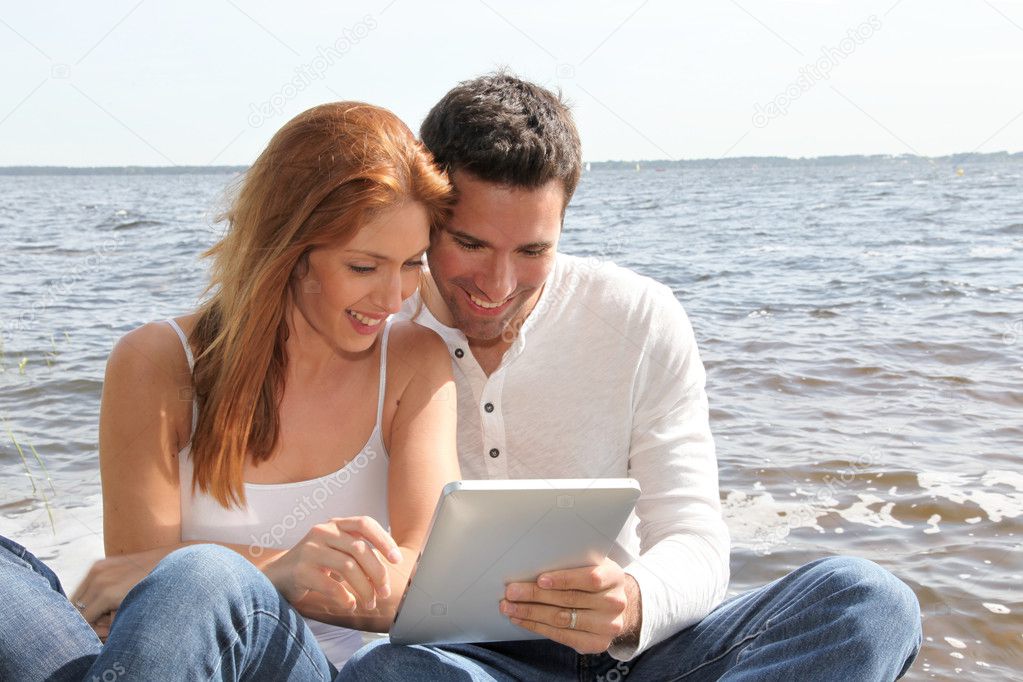 Couple using electronic tablet by a lake