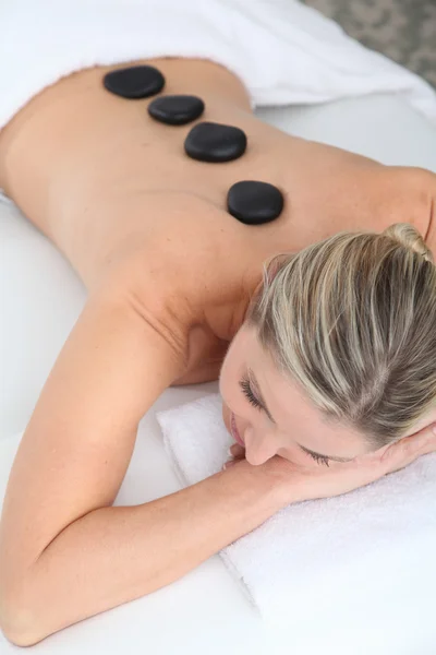 Mulher deitada na cama de massagem com pedras quentes nas costas — Fotografia de Stock