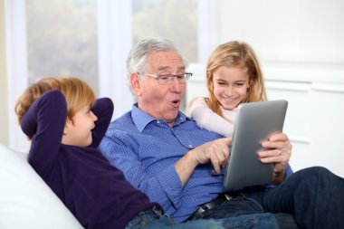 Grandfather with kids using electronic tab clipart