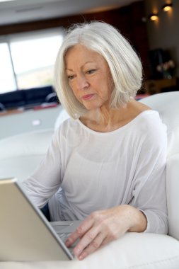 Senior woman surfing on internet at home clipart