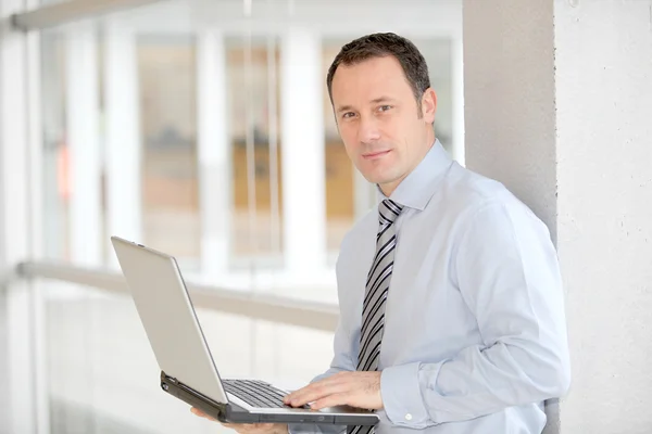 Empresário de pé no hall com computador portátil — Fotografia de Stock