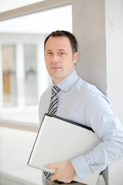 Biznesmen stoi w hali z laptopa — Zdjęcie stockowe