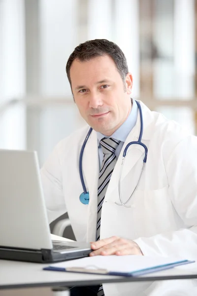 Доктор сидит за своим столом с ноутбуком — стоковое фото