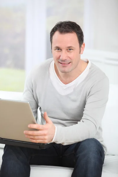 Człowiek siedzi w kanapie przy użyciu komputera przenośnego — Zdjęcie stockowe