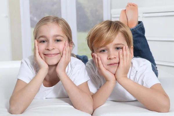 Blond children laying in sofa with hands on chin — Stock Photo, Image