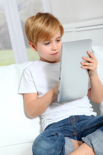 Mały chłopiec siedzi w kanapie z elektronicznych tabletki — Zdjęcie stockowe