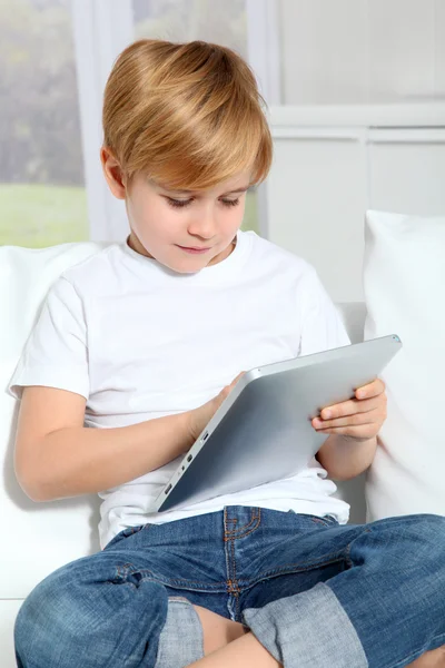 Niño sentado en sofá con tableta electrónica — Foto de Stock