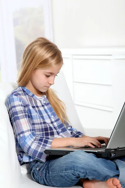 Piccola ragazza bionda seduta sul divano con computer portatile — Foto Stock
