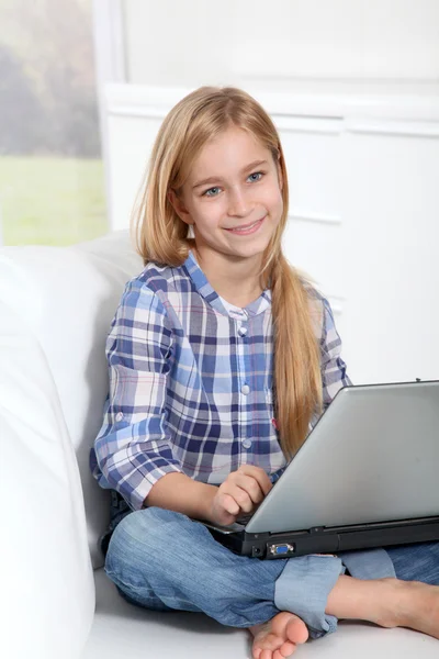 Piccola ragazza bionda seduta sul divano con computer portatile — Foto Stock