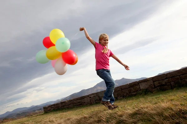 Little girl holding balloons out in the countryside — Stock Photo, Image