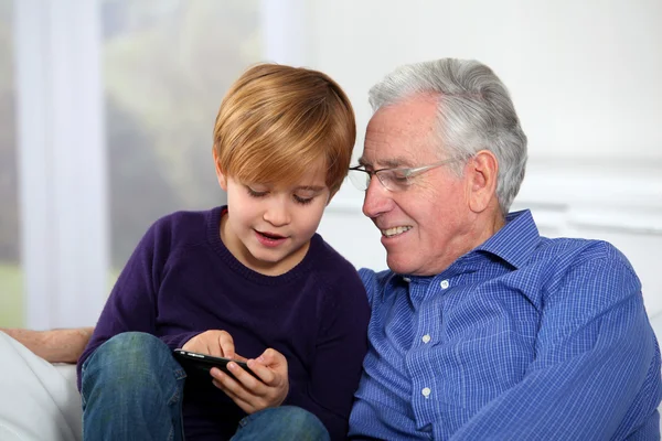 Старик с маленьким мальчиком играет в видеоигры по телефону — стоковое фото