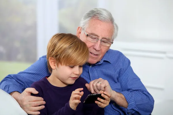 Старик с маленьким мальчиком играет в видеоигры по телефону — стоковое фото